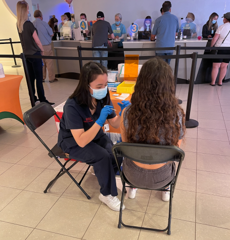 Junior Lourdes Castruita receives her first dose of the Pfizer Vaccine at the Grossmont Sharp Clinic. In the background other people wait to get their vaccines.

