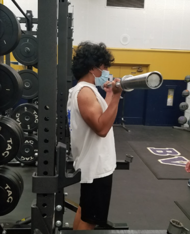 Junior Kevin Ituriaga  works on building his  bicep muscles by completing bar curls. This took place during BVHs boys volleyball preseason strength and training camp. 