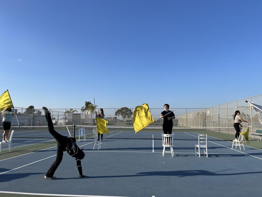 Winterguard members rehearse on BVHs tennis courts. Several students dance while others flip flags in order to create a cohesive performance.