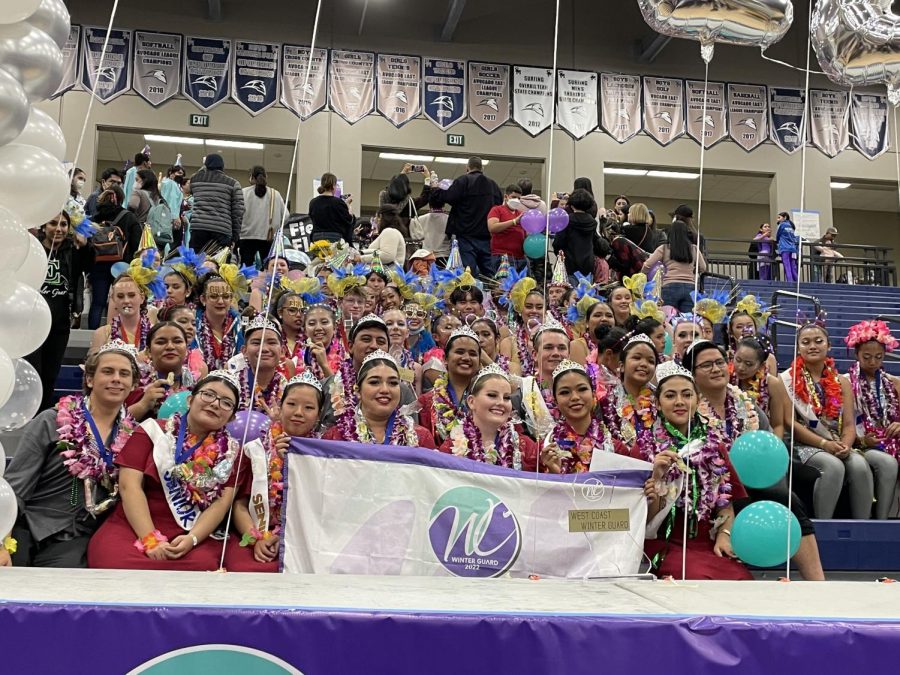 Winterguard holds a banner honoring their first place victory for their performance titled The Waiting Game. The group sits with their sister schools after awards were announced at the SMWC Winterguard Championship.