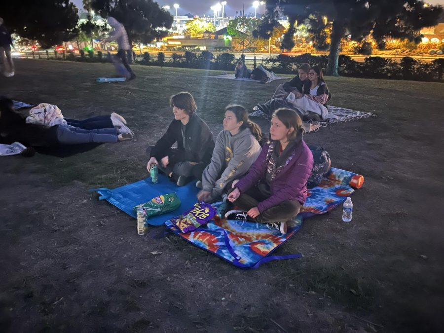 Junior Aiden Koenig, sophomore Natalie Lewis and sophomore Amelia Roy sit together and enjoy as Home Alone opens on the screen. Many students bring their own blankets to sit on in the cold.