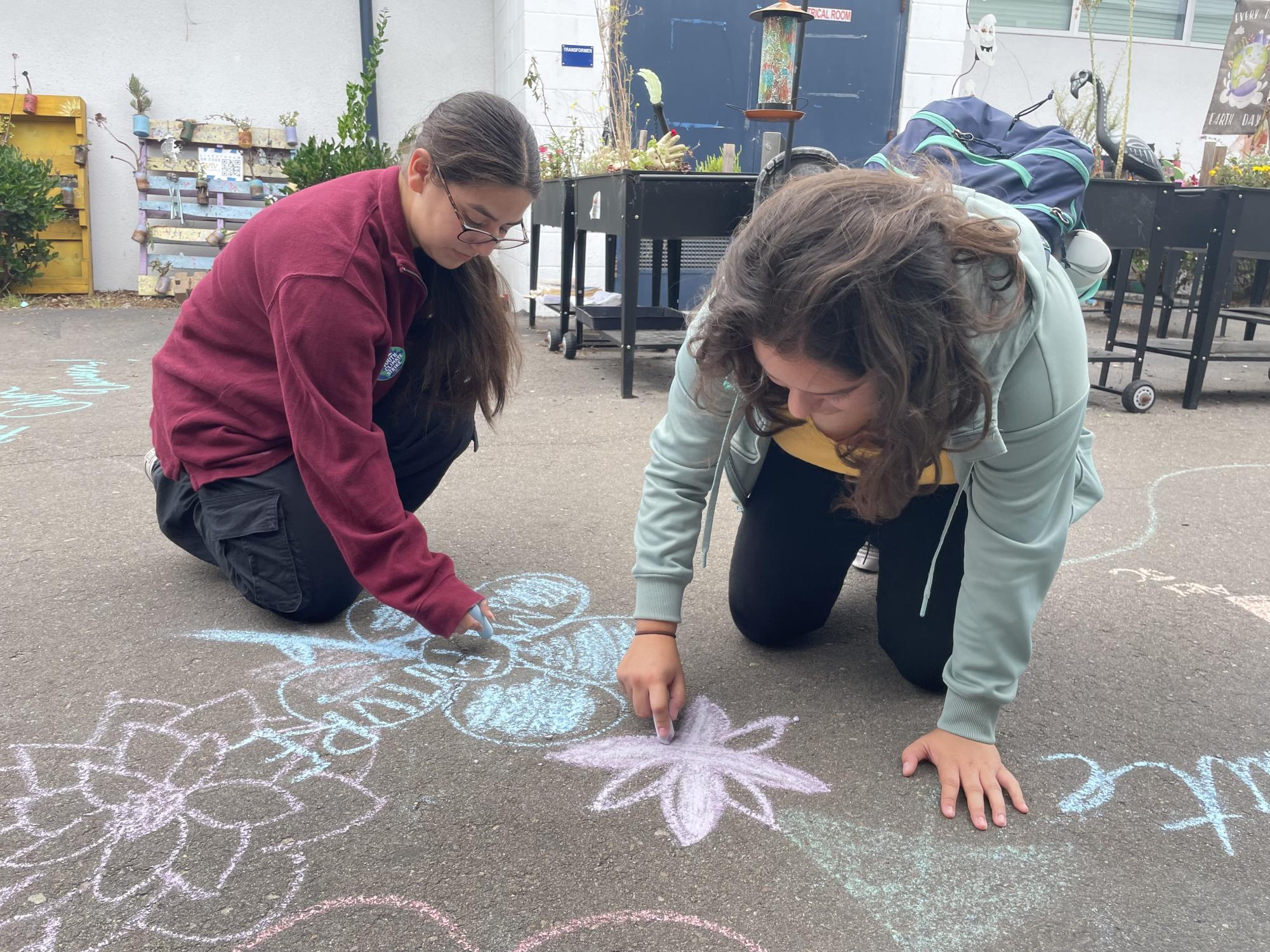 Green Team and Y4SF president Aaliyah Victoria (left) demonstrates Climate Change week activity during lunch, sketching colorful art on the blacktop. Erica Palacios (right) joins Victoria in the activity.