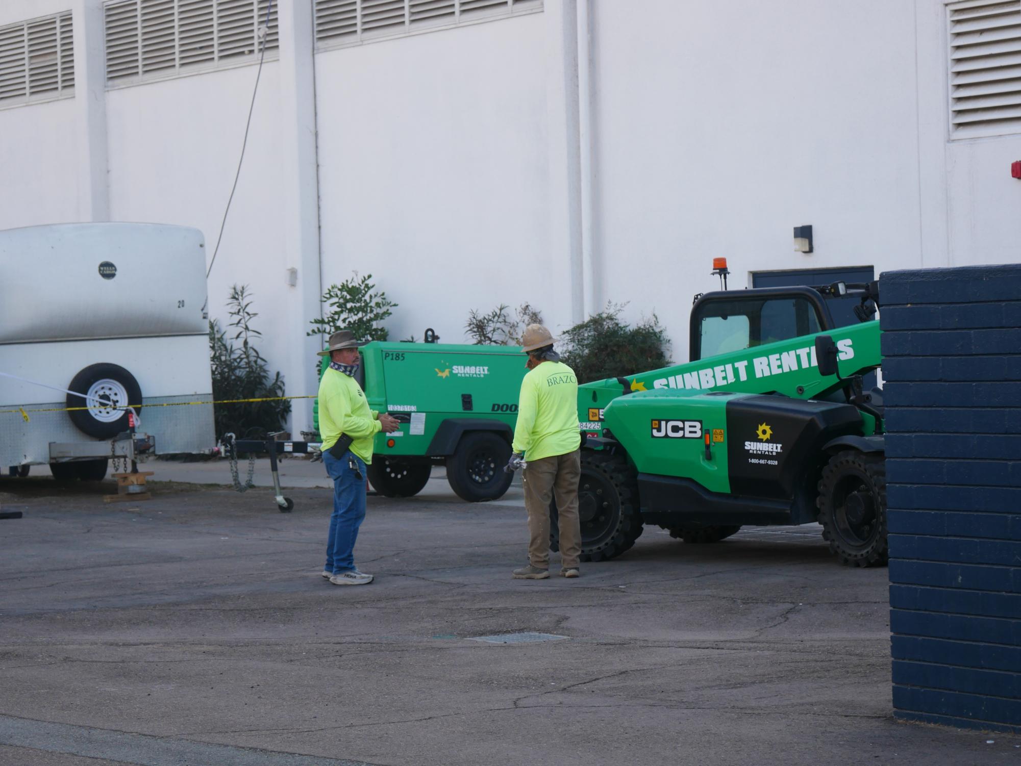 Two workers discuss plans for construction near the BVH gym. They soon return to work atop the roof.