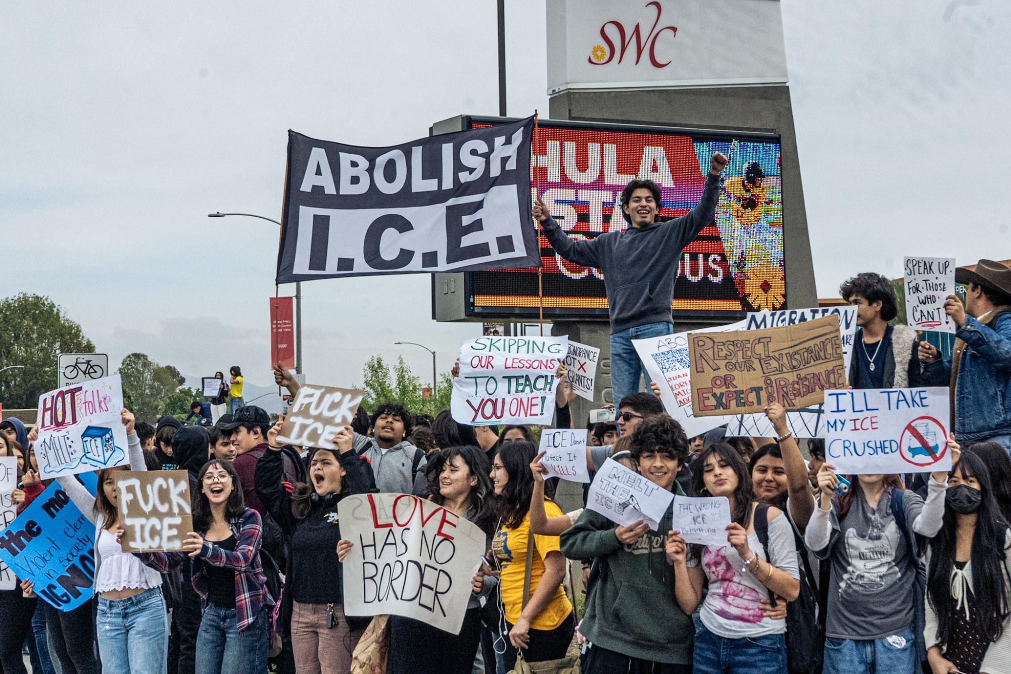 Protesters gathered across the street from BVHS near SWC, some climbing onto electrical boxes to make their signs visible.