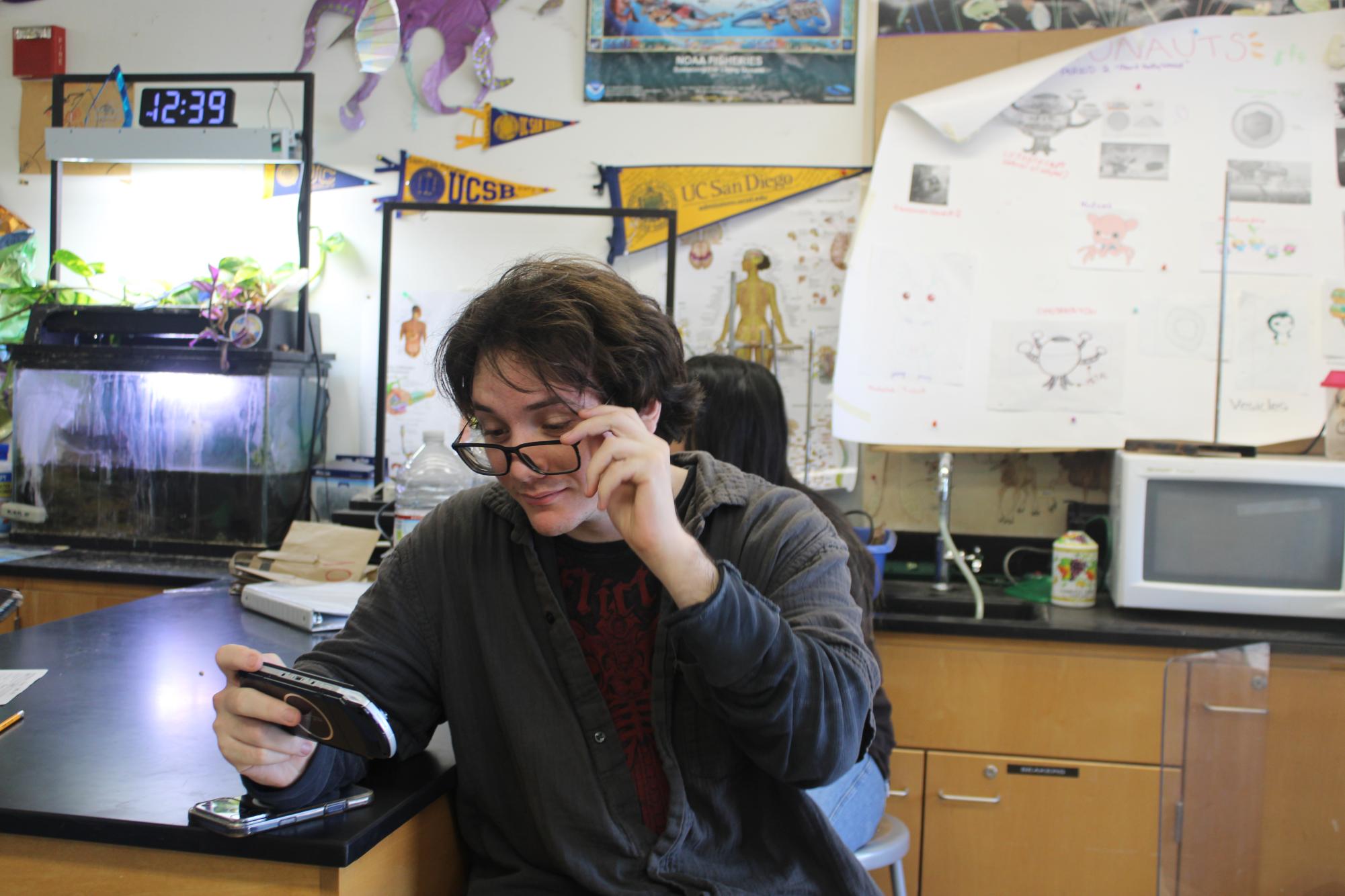 Senior Giovanni George is seen in room 401 adjusting his glasses while playing on his phone.
